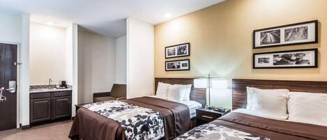 Habitación de hotel con dos camas, un escritorio, una silla, un lavamanos y cuadros en la pared.