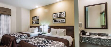 Habitación de hotel con dos camas, un espejo grande, tocador con lavamanos y cuadros en la pared.