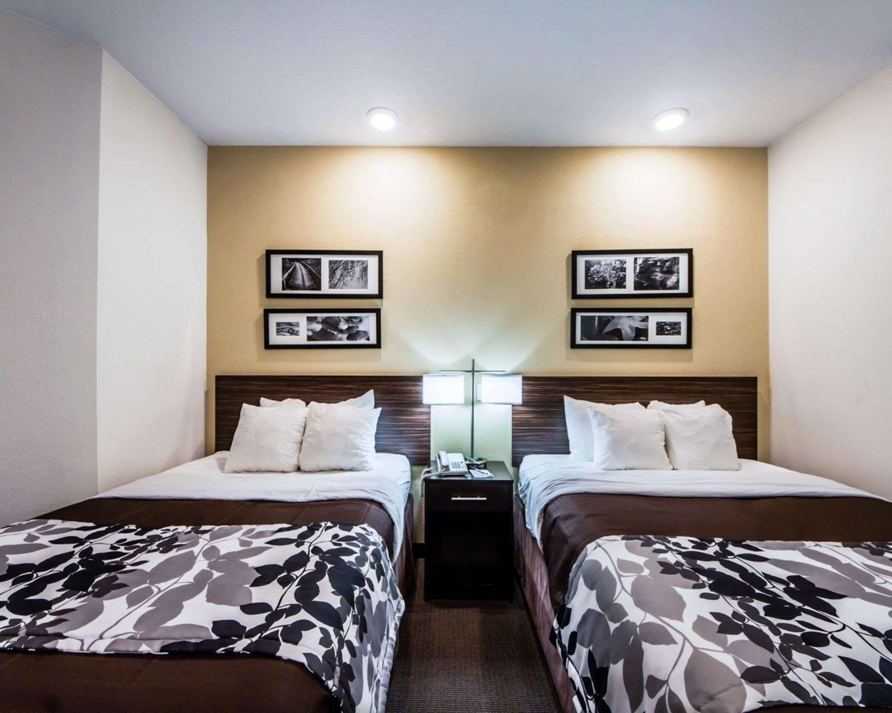 A hotel room with two beds, a nightstand with a lamp, and two framed pictures on the wall.
