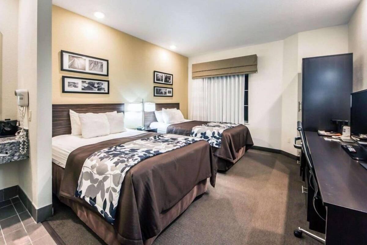 Ett hotellrum med två sängar, ett skrivbord, en tv och inramade tavlor på väggen.