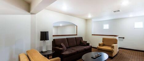 A hotel room with a brown sofa, two armchairs, a small table, and a lamp.