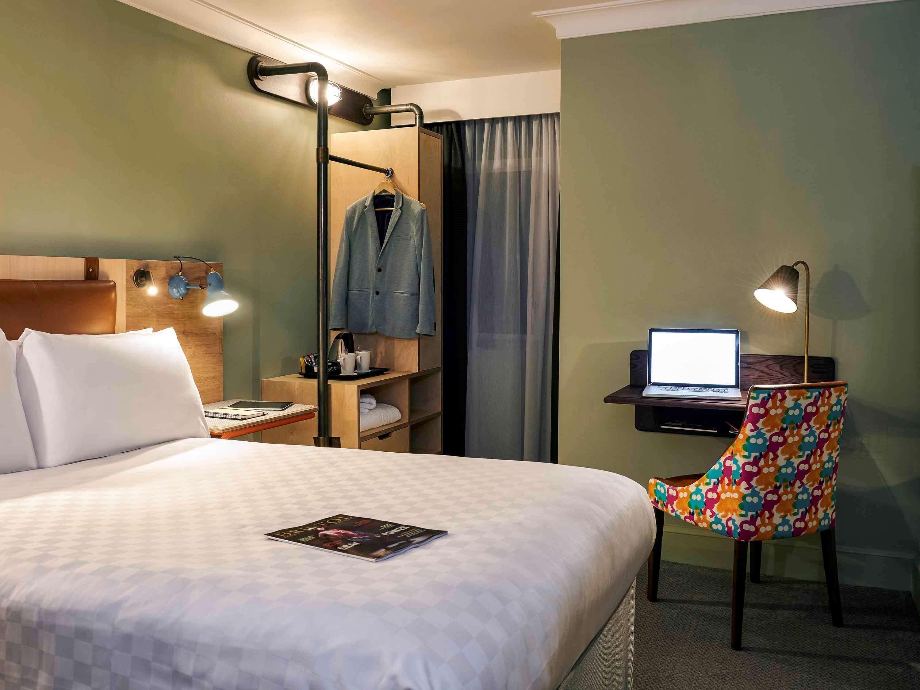 Hotelkamer met een bed, bureau met een laptop, stoel, kapstok en plank met een jas.