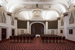 Meetings take place in this elegant conference room with a central stage, ornate columns, and a detailed ceiling.