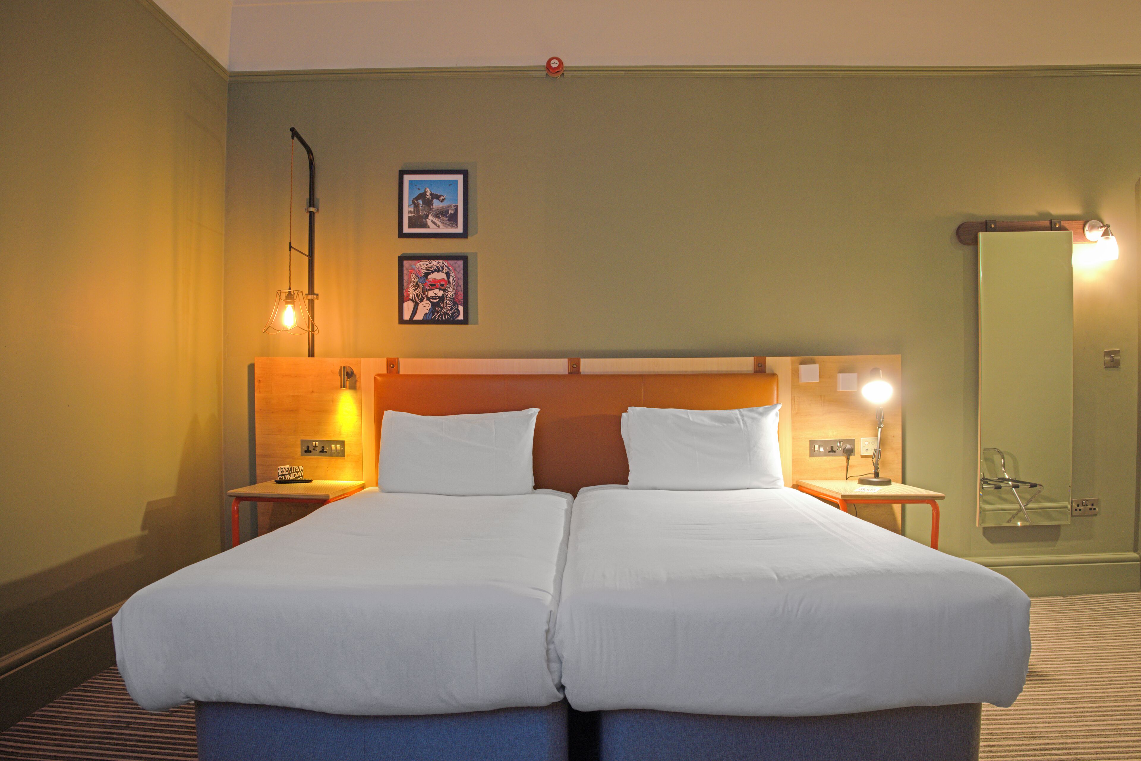 Un lit double avec du linge de lit blanc, deux tables de chevet avec des lampes et deux tableaux encadrés au mur.