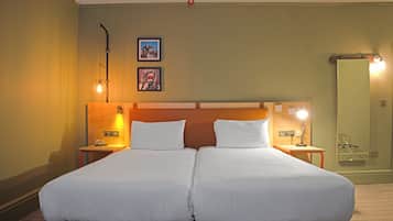 Una cama doble con ropa blanca, dos mesitas de noche con lámparas y dos cuadros en la pared.