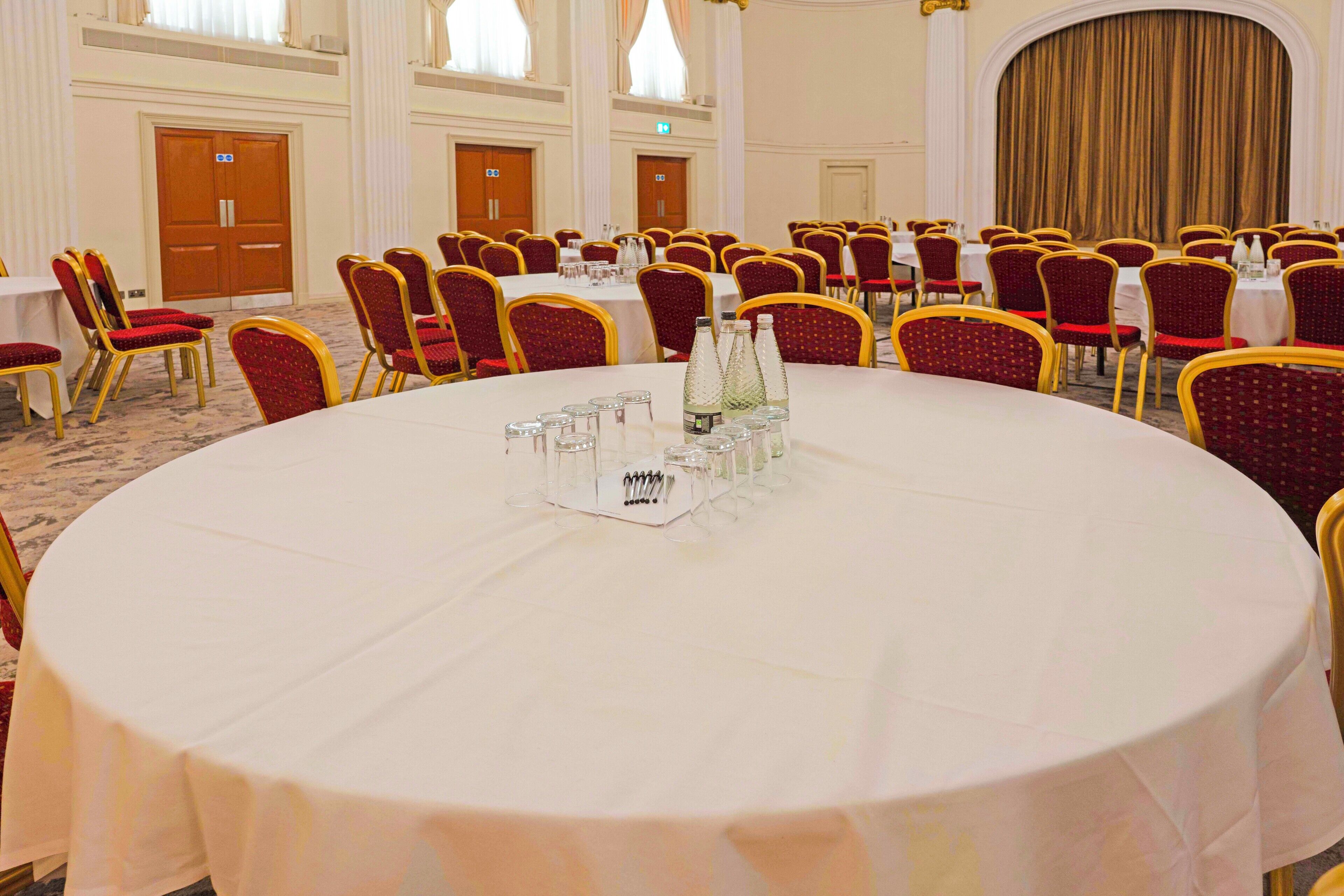 A conference room with round tables, red and gold chairs, and a white tablecloth.