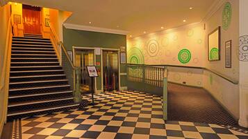 Un hall d’hôtel avec un sol à carreaux, un escalier et un comptoir d’accueil.