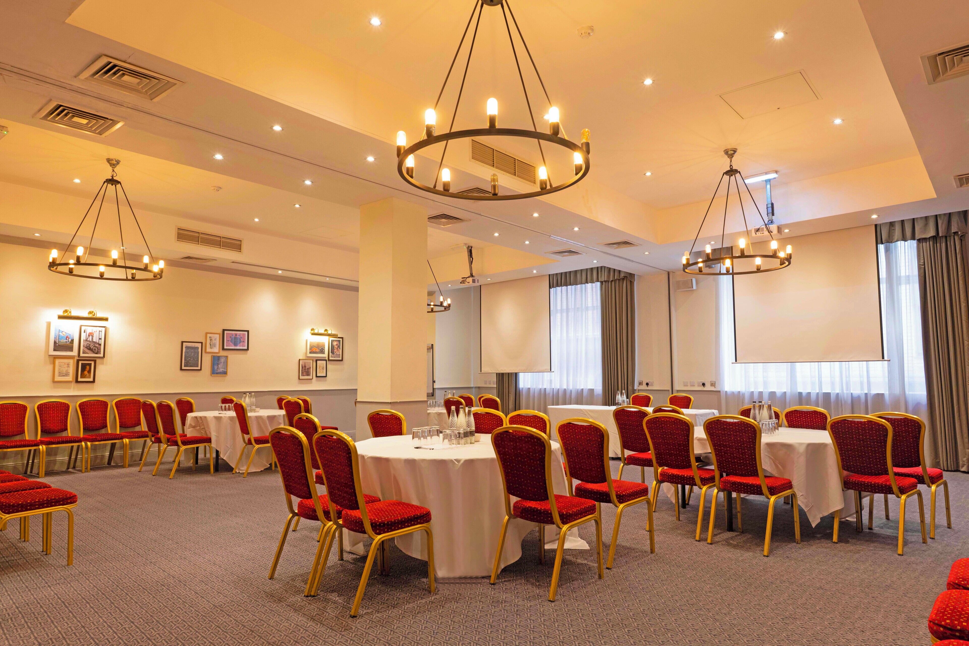 A conference room with round tables, red chairs, and chandeliers.