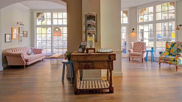 Una habitación amplia con suelo de madera, un sofá rosa, una mesa de centro de madera y un sillón colorido.