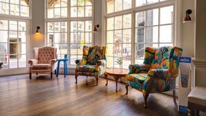 Una habitación amplia con ventanas grandes, suelo de madera y una mezcla de sillones clásicos y coloridos.