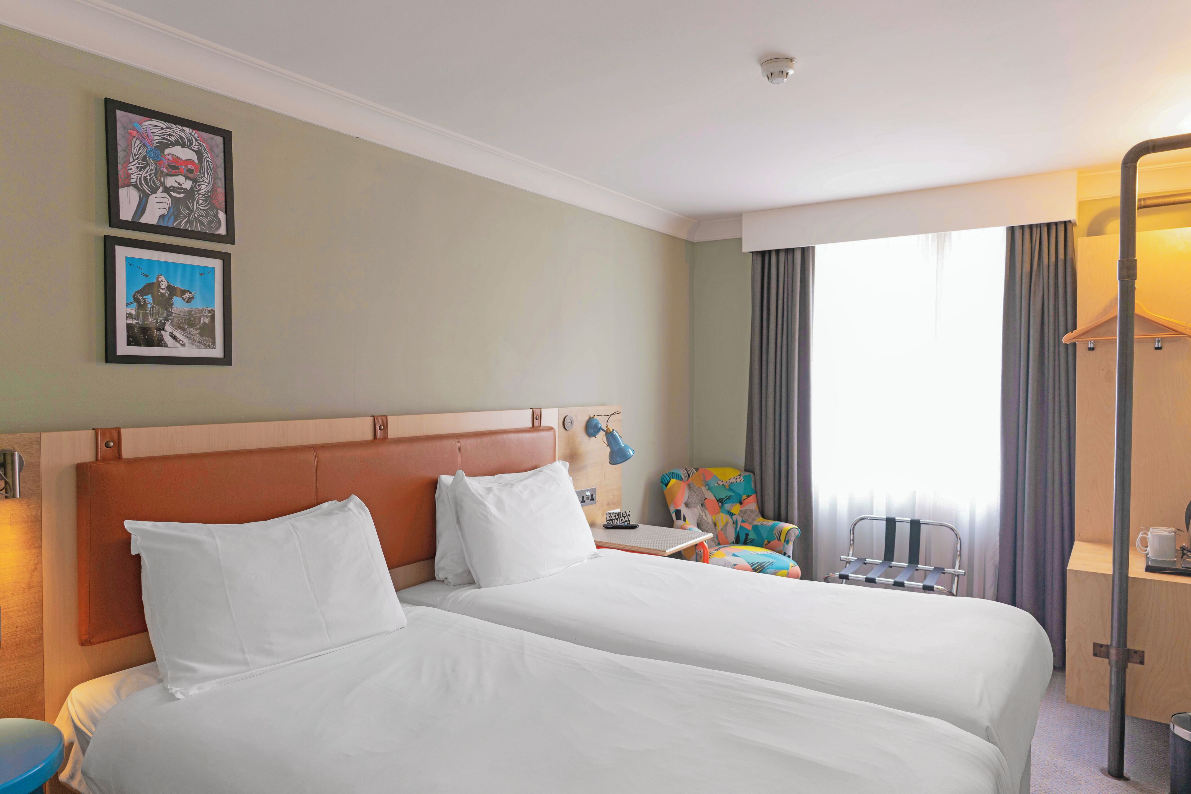 A hotel room with two beds, a desk, a chair, and a window with curtains.
