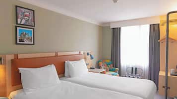 Habitación de hotel con dos camas, un escritorio, una silla y una ventana con cortinas.