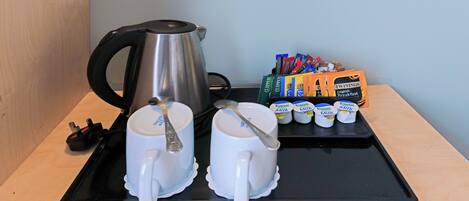 A tray with two white mugs, a silver kettle, and a set of Twinings English Breakfast tea packets.