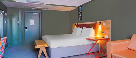 A modern hotel room with a bed, a small table, a chair, and a sofa.