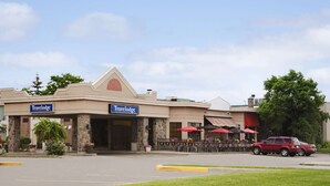 A Travelodge hotel with a stone facade, outdoor seating area, and a red car parked in front.