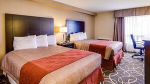A hotel room with two beds, a desk, a chair, and a window with curtains.