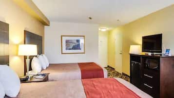 A hotel room with two beds, a television, a desk with a lamp, and a framed picture on the wall.