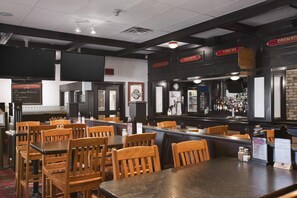 A bar area with wooden tables and chairs, a bar counter, and a selection of liquor bottles. - Travelodge by Wyndham Cambridge - Waterloo (Cambridge)