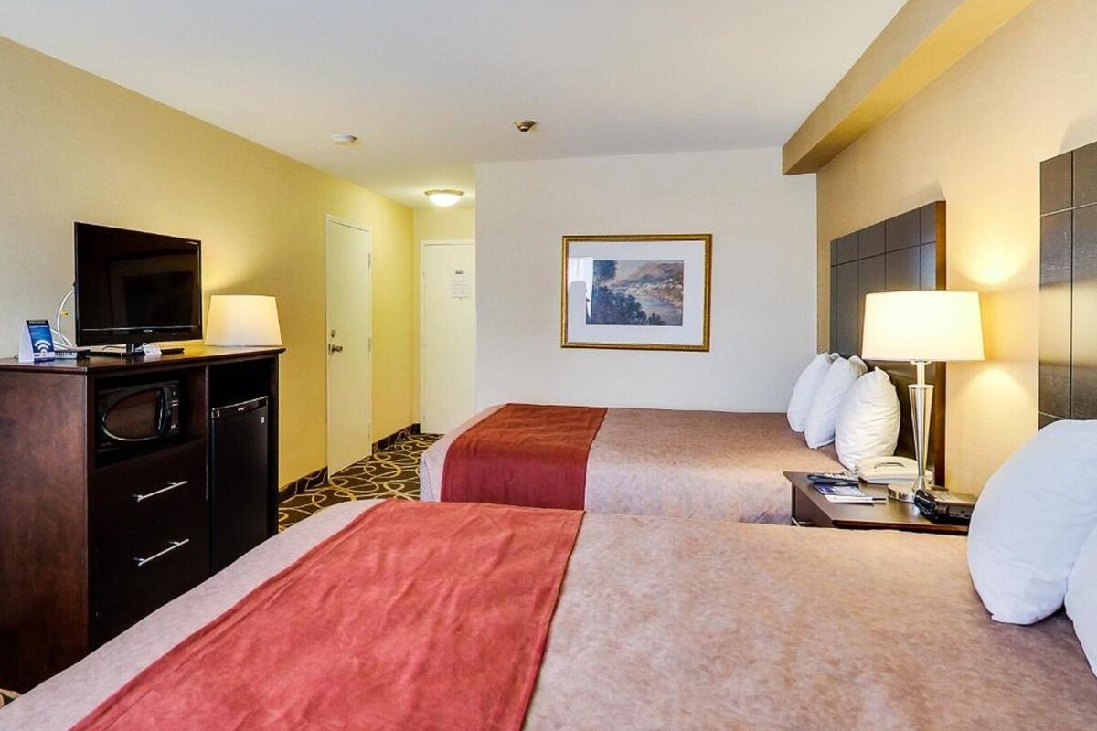 A hotel room with two beds, a TV, a desk, and a painting on the wall.