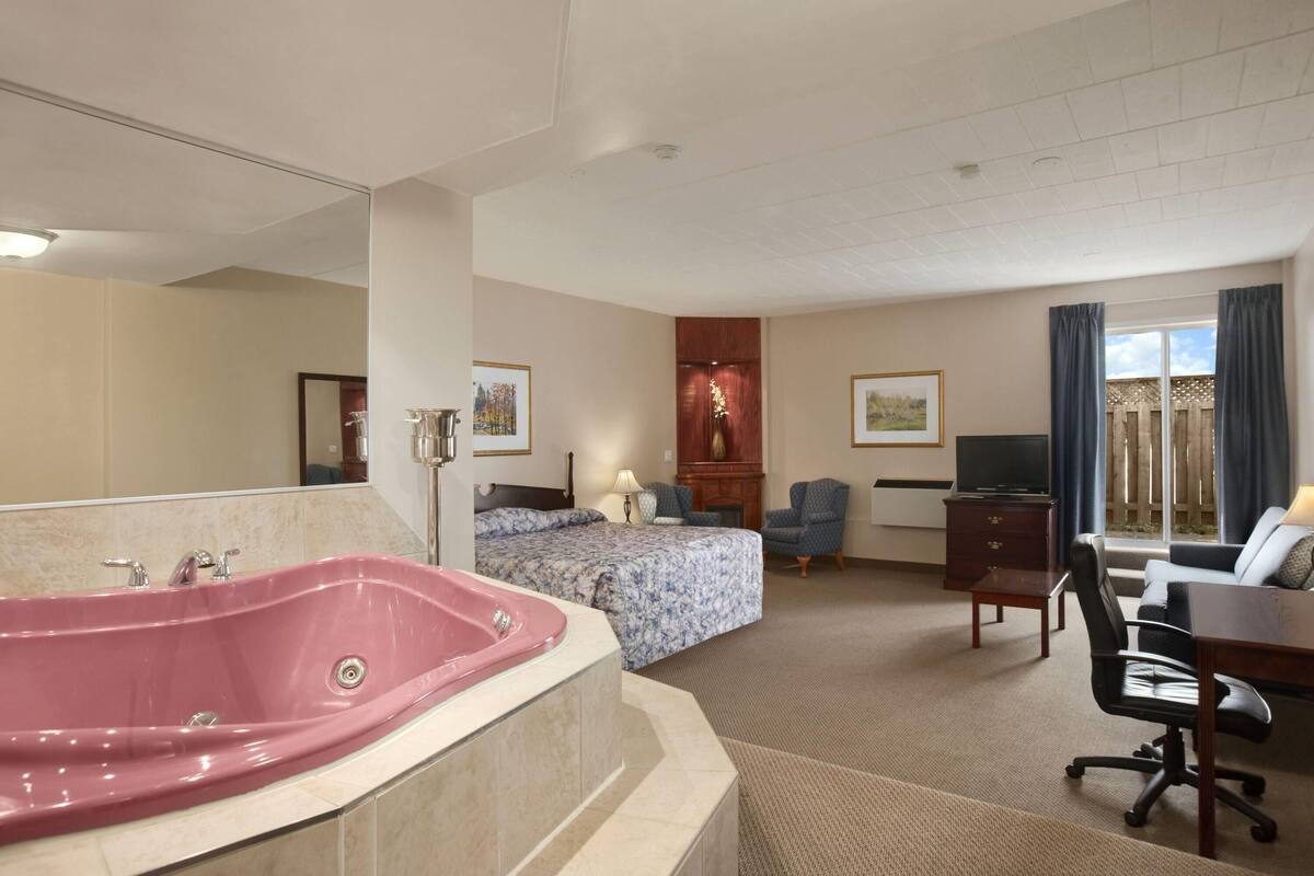 Habitación de hotel con una bañera grande, cama con colcha estampada, escritorio y televisor.