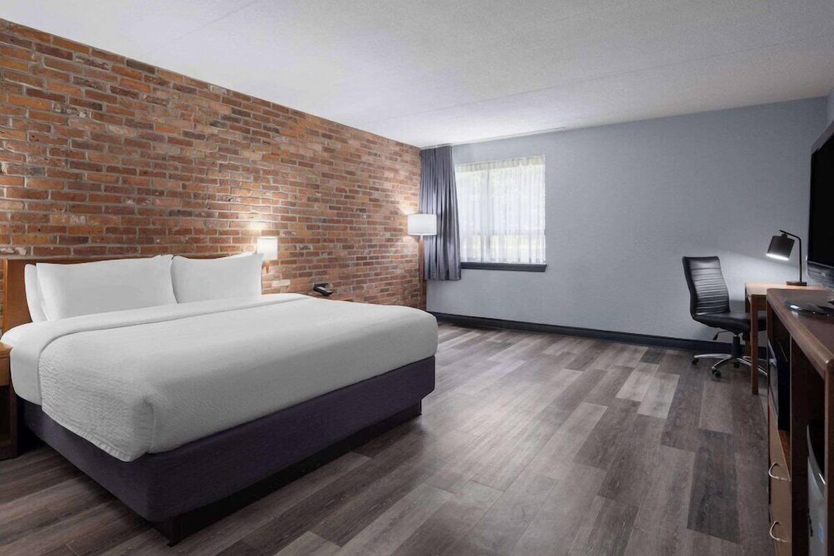 Une chambre d’hôtel avec un mur décoratif en briques, un lit, un bureau avec une chaise, une télévision et une fenêtre avec des rideaux.