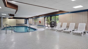 En inomhuspool med ett kaklat golv, en poolstege och vita solstolar längs väggen.
