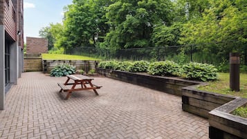 A paved patio with a wooden picnic table and raised garden beds with plants.