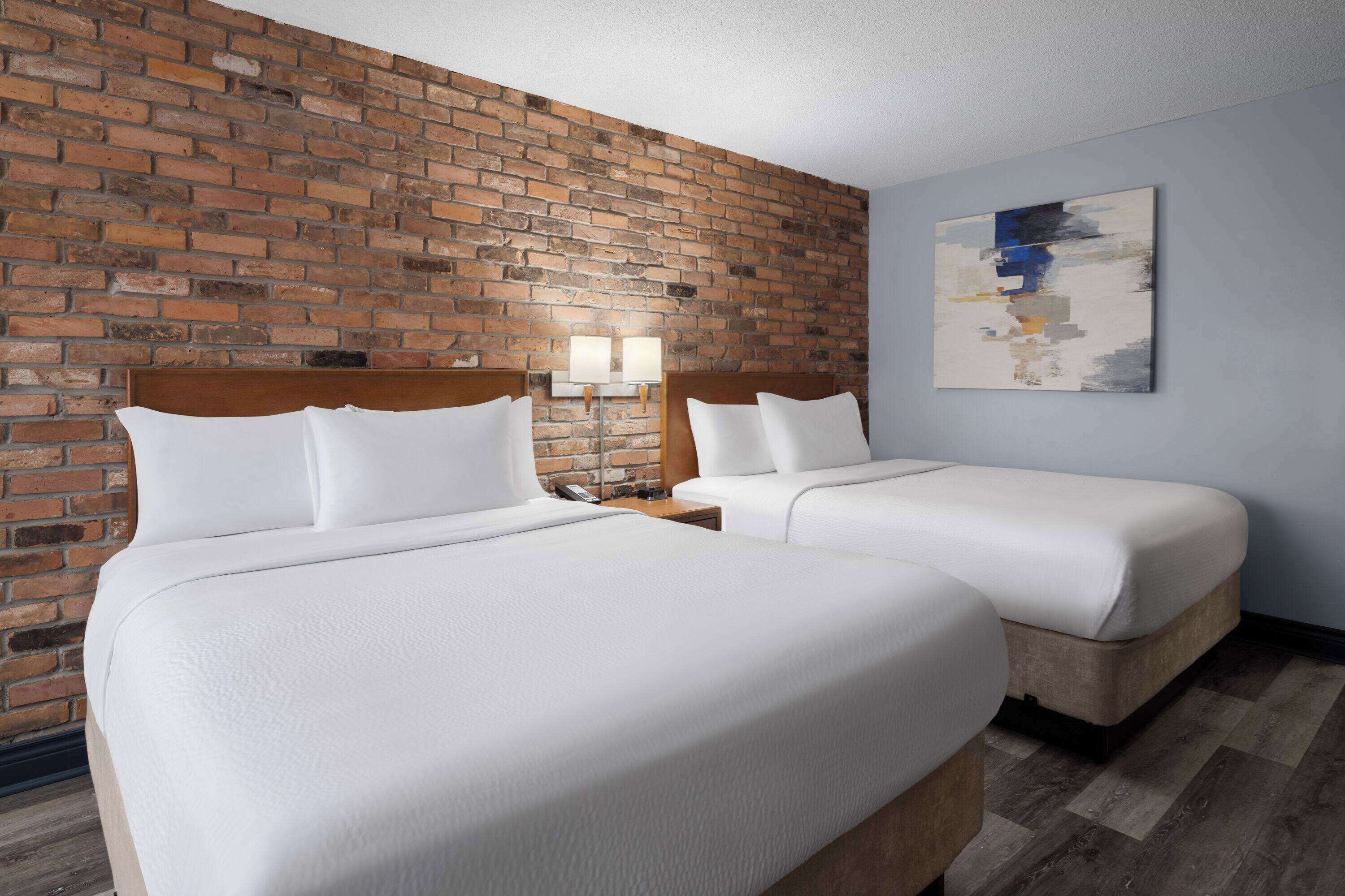 Ein Hotelzimmer mit zwei Betten, einer Ziegelwand, einem modernen abstrakten Gemälde und einem Holzboden.