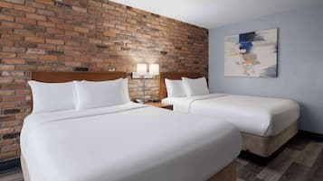 A hotel room with two beds, a brick wall, a modern abstract painting, and a wooden floor.
