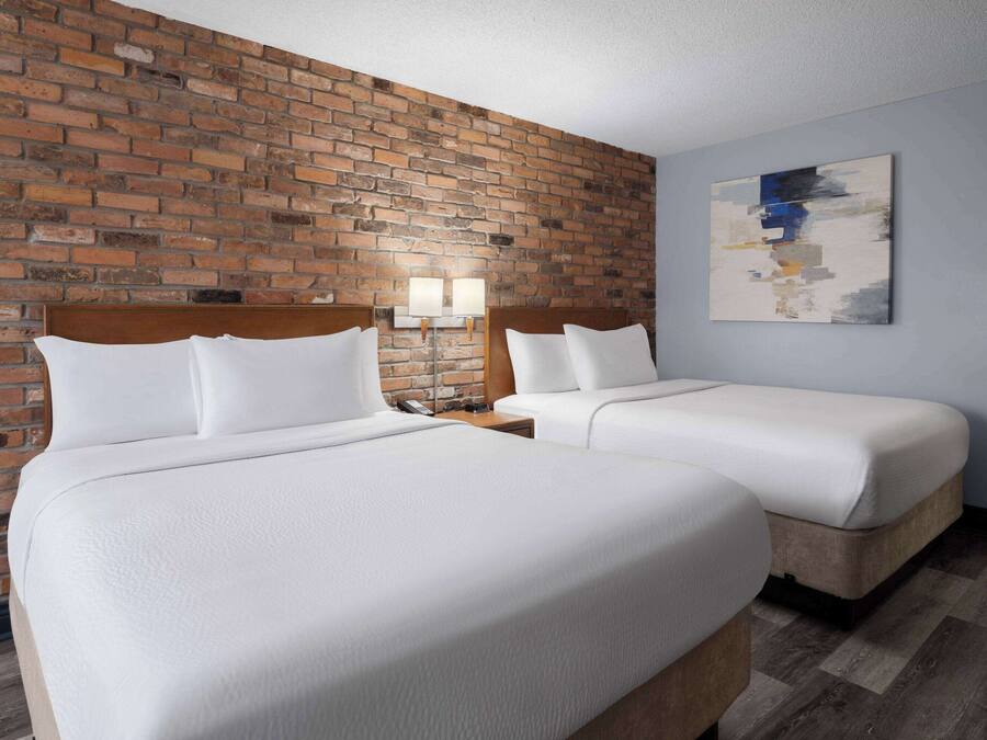 A hotel room with two beds, a brick wall, a modern abstract painting, and a wooden floor.