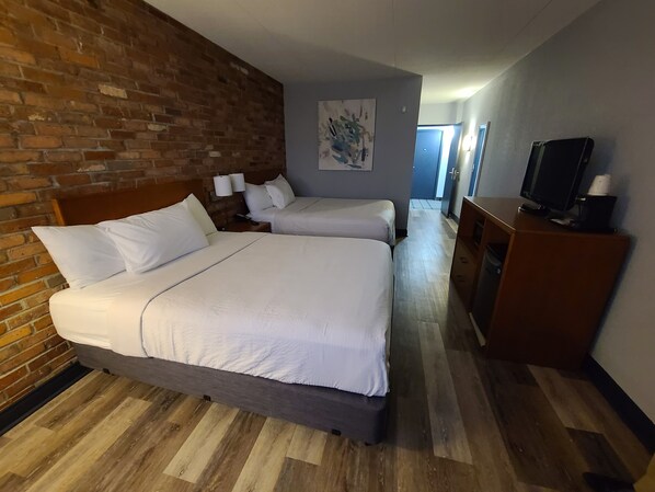 A hotel room with two beds, a brick wall, a painting, a TV, and a wooden dresser.