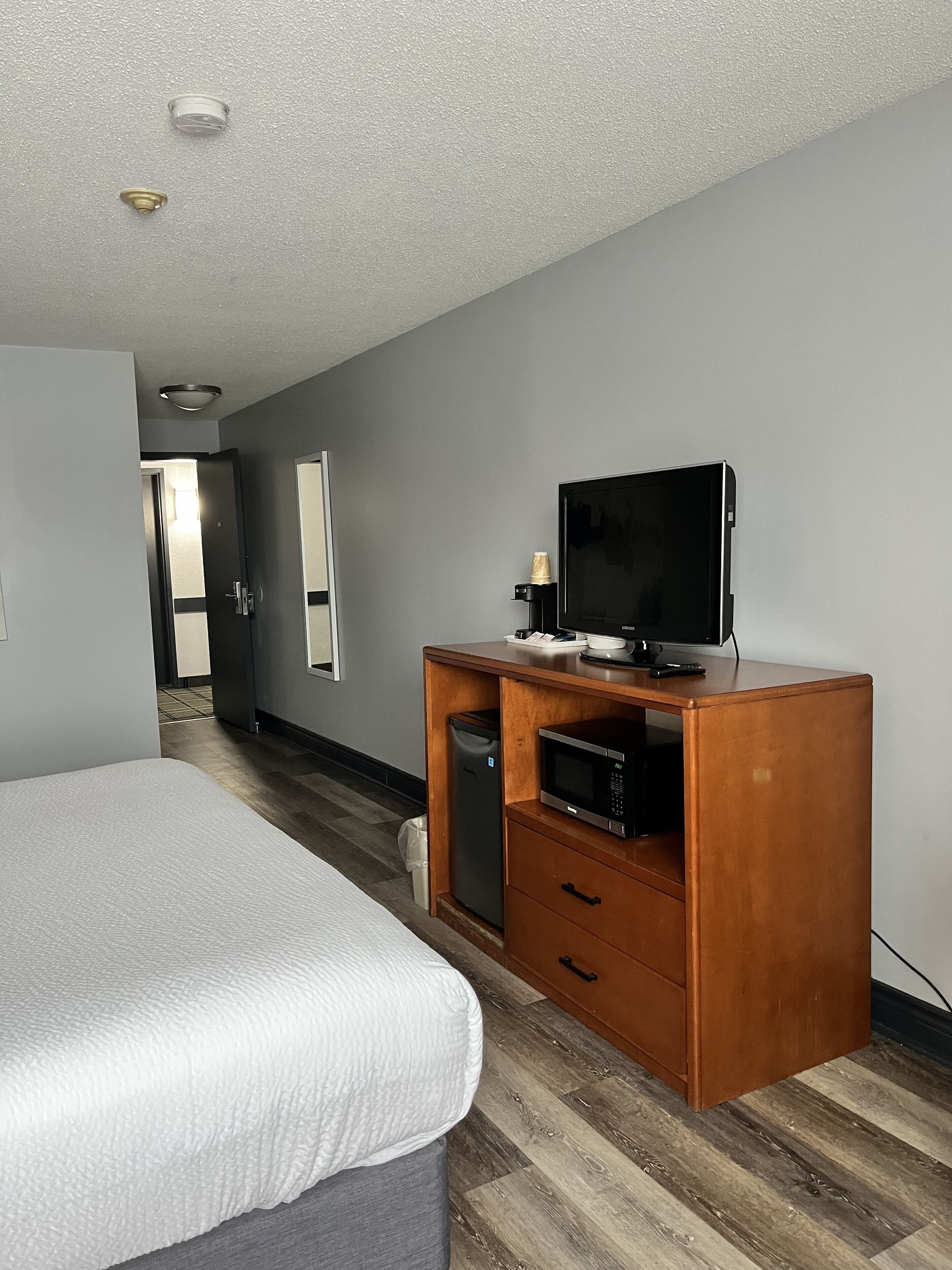A hotel room with a bed, a wooden desk with a television, a microwave, and a small refrigerator.