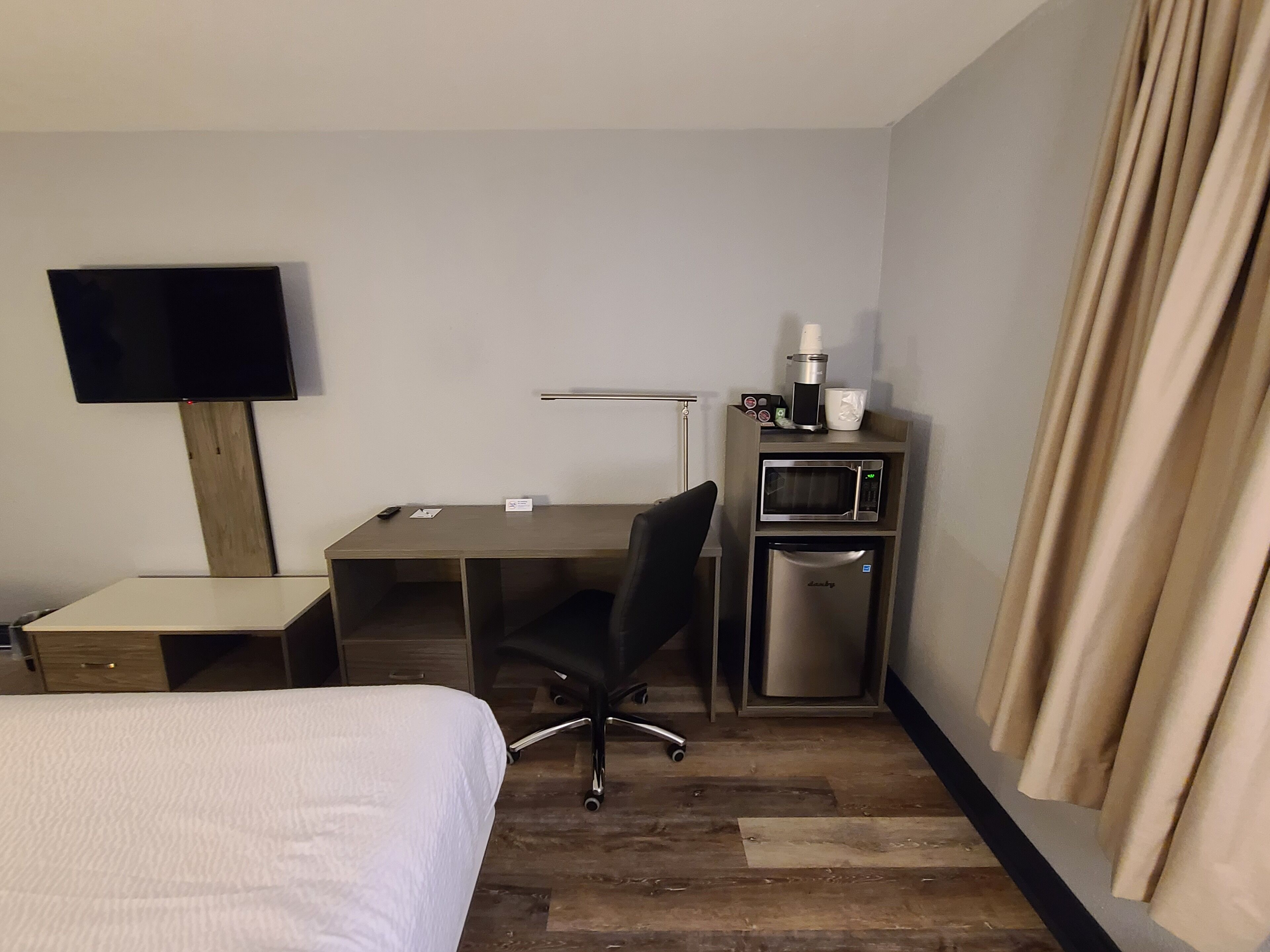 A hotel room with a bed, a desk, a chair, a television, a microwave, and a coffee maker.