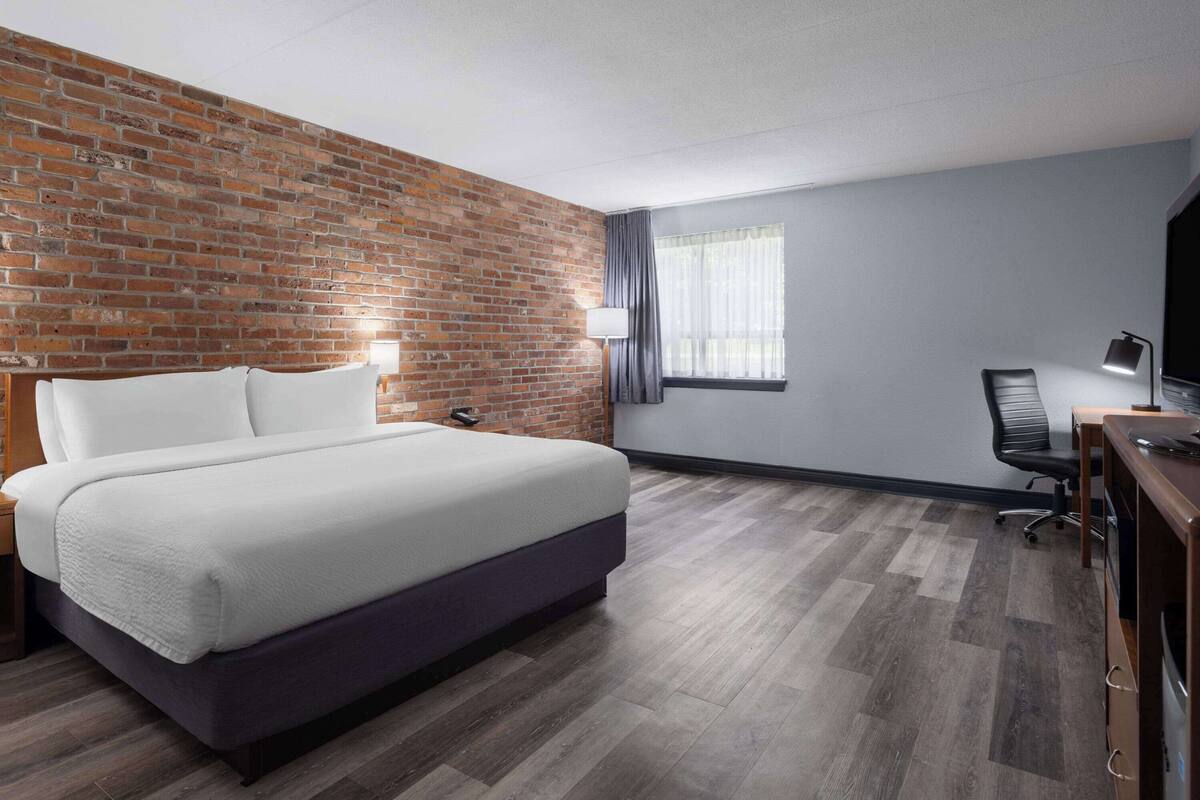 Une chambre d’hôtel avec un mur d’accent en briques, un lit, un bureau avec une chaise et une fenêtre avec des rideaux.