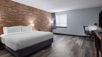 Ein Hotelzimmer mit einer Wand aus Ziegelsteinen, einem Bett, einem Schreibtisch mit Stuhl und einem Vorhangfenster.