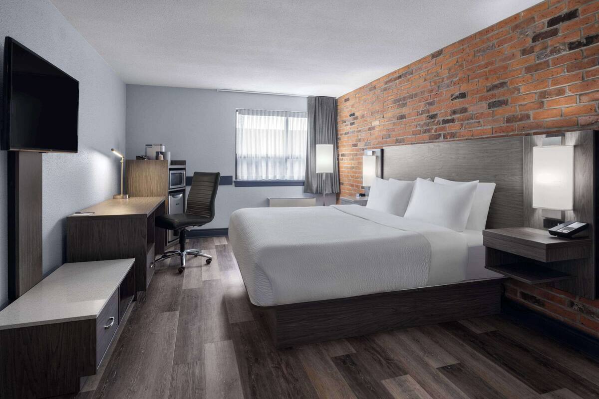 Une chambre d’hôtel avec un grand lit, un bureau, une télévision, une lampe de bureau, une chaise et un mur en briques.