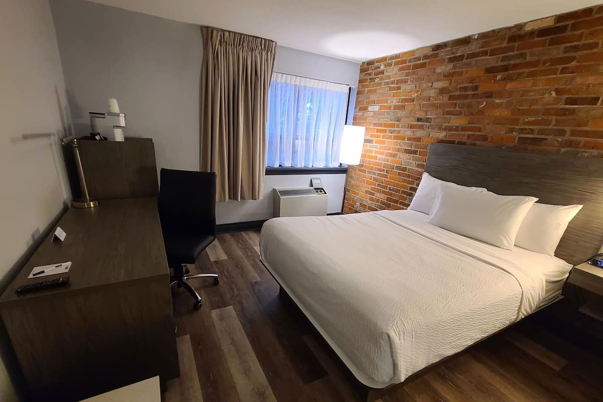 Une chambre d’hôtel avec un lit, un bureau, une chaise et un mur en briques.