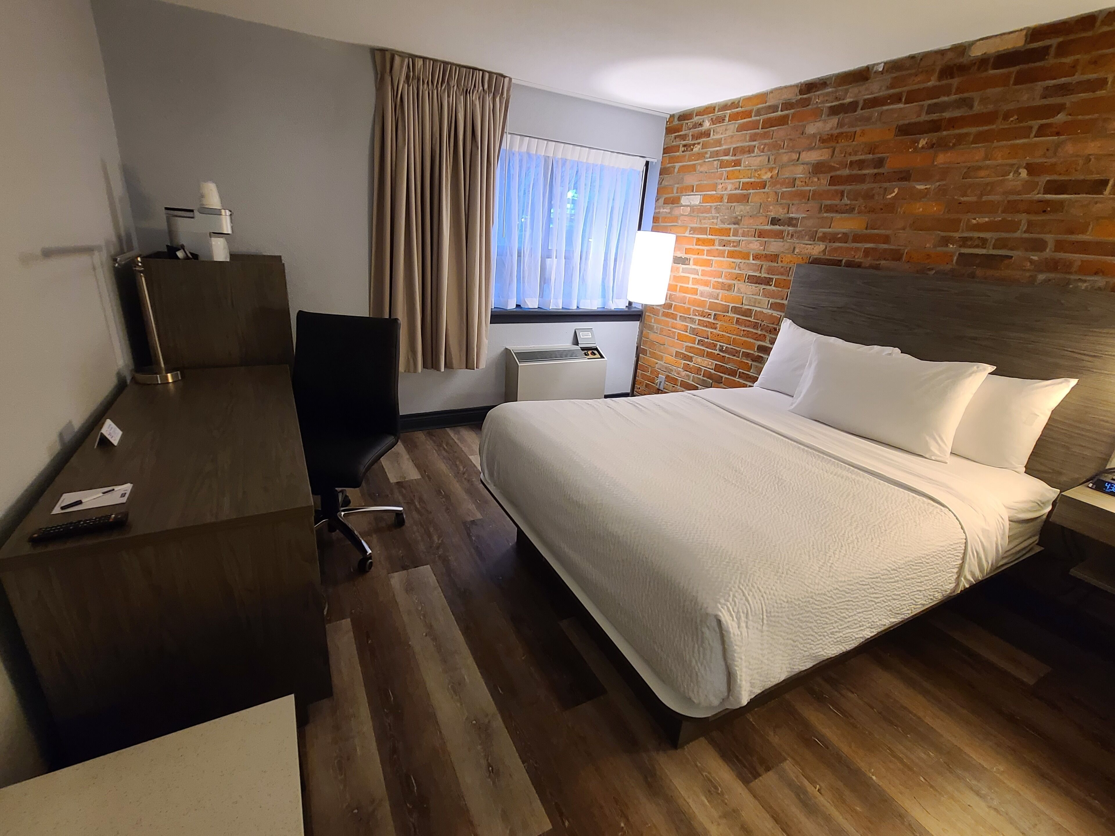 Habitación de hotel con una cama, un escritorio, una silla, un televisor y una pared de ladrillo.