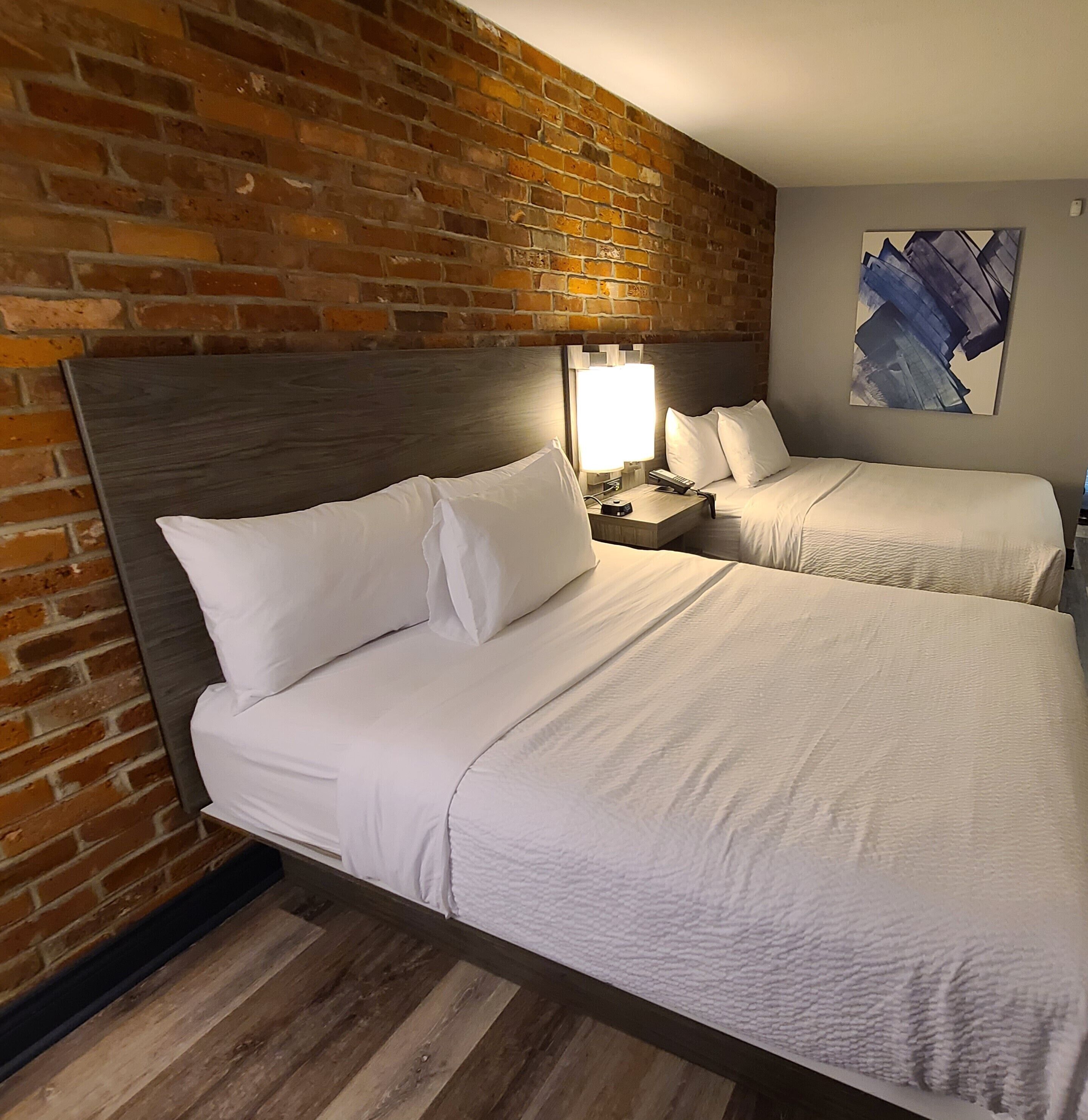 Una habitación de hotel con dos camas, un muro de ladrillo y un cuadro en la pared.