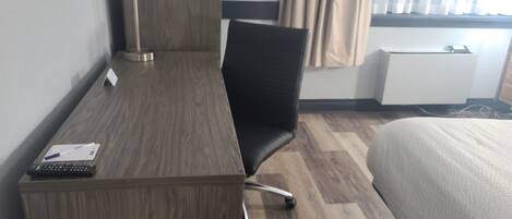 Une chambre d’hôtel avec un bureau en bois, une chaise de bureau noire, un lit et une fenêtre avec des rideaux.