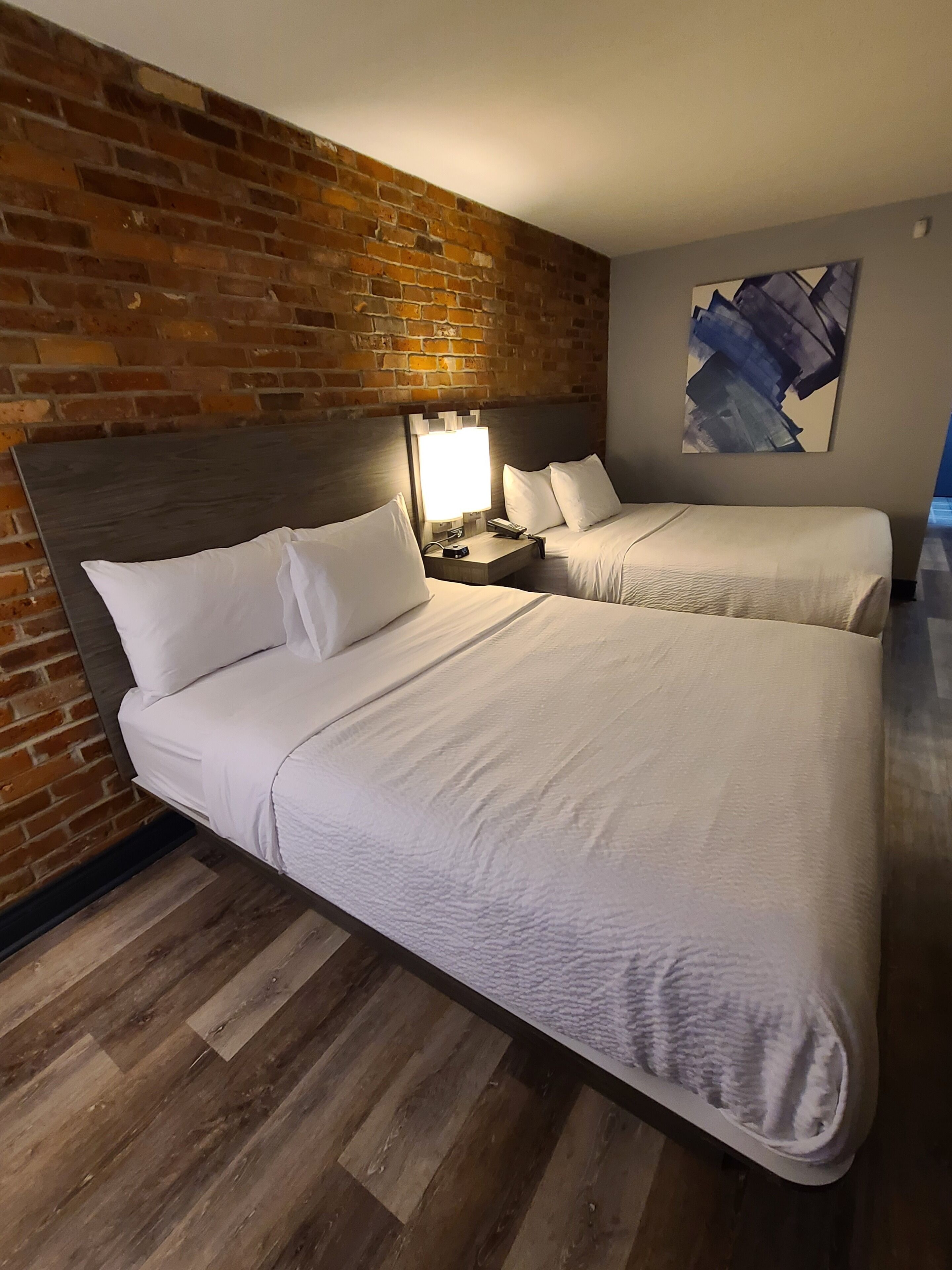 Een hotelkamer met twee bedden, een bakstenen muur, een modern schilderij en een houten vloer.