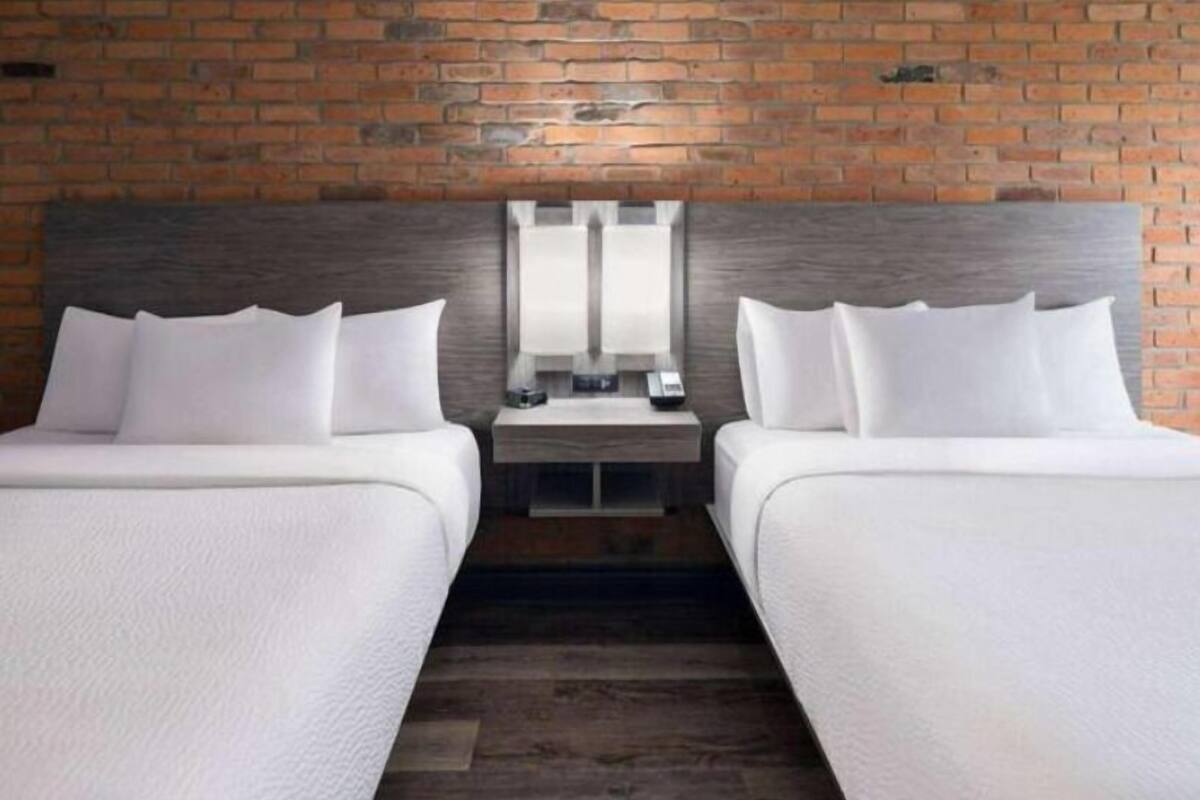 Une chambre d’hôtel avec deux lits, un mur en briques et une tête de lit en bois.