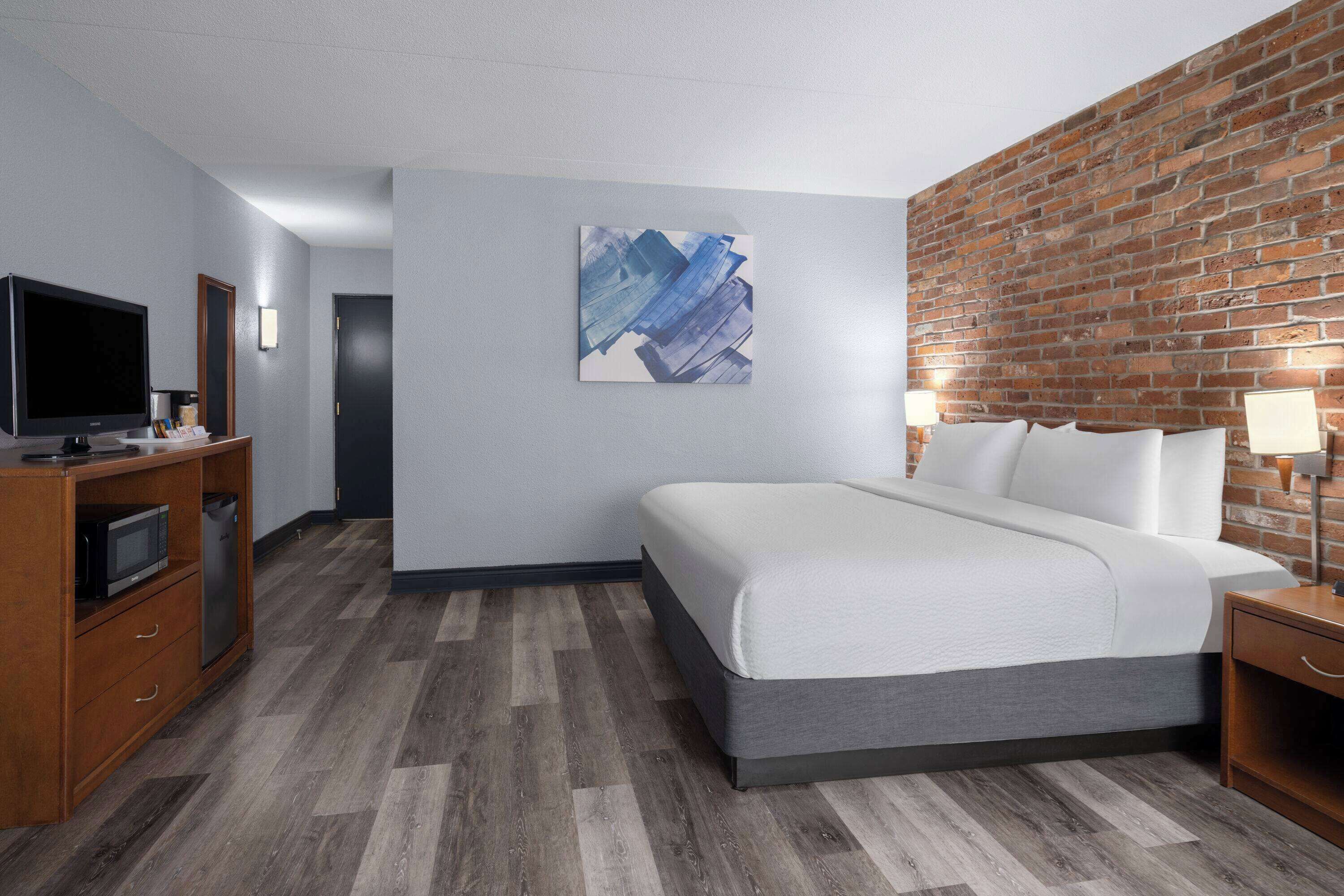 A hotel room with a bed, a television, a desk, and a brick wall.