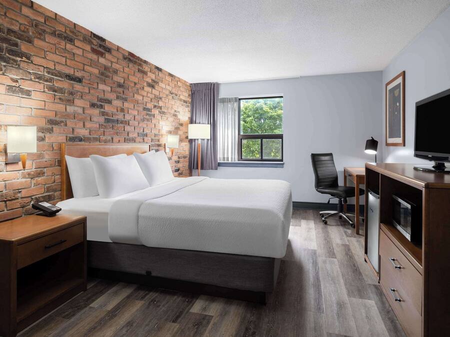 Une chambre d’hôtel avec un mur en briques, un grand lit, un bureau avec une télévision et une fenêtre donnant sur des arbres.