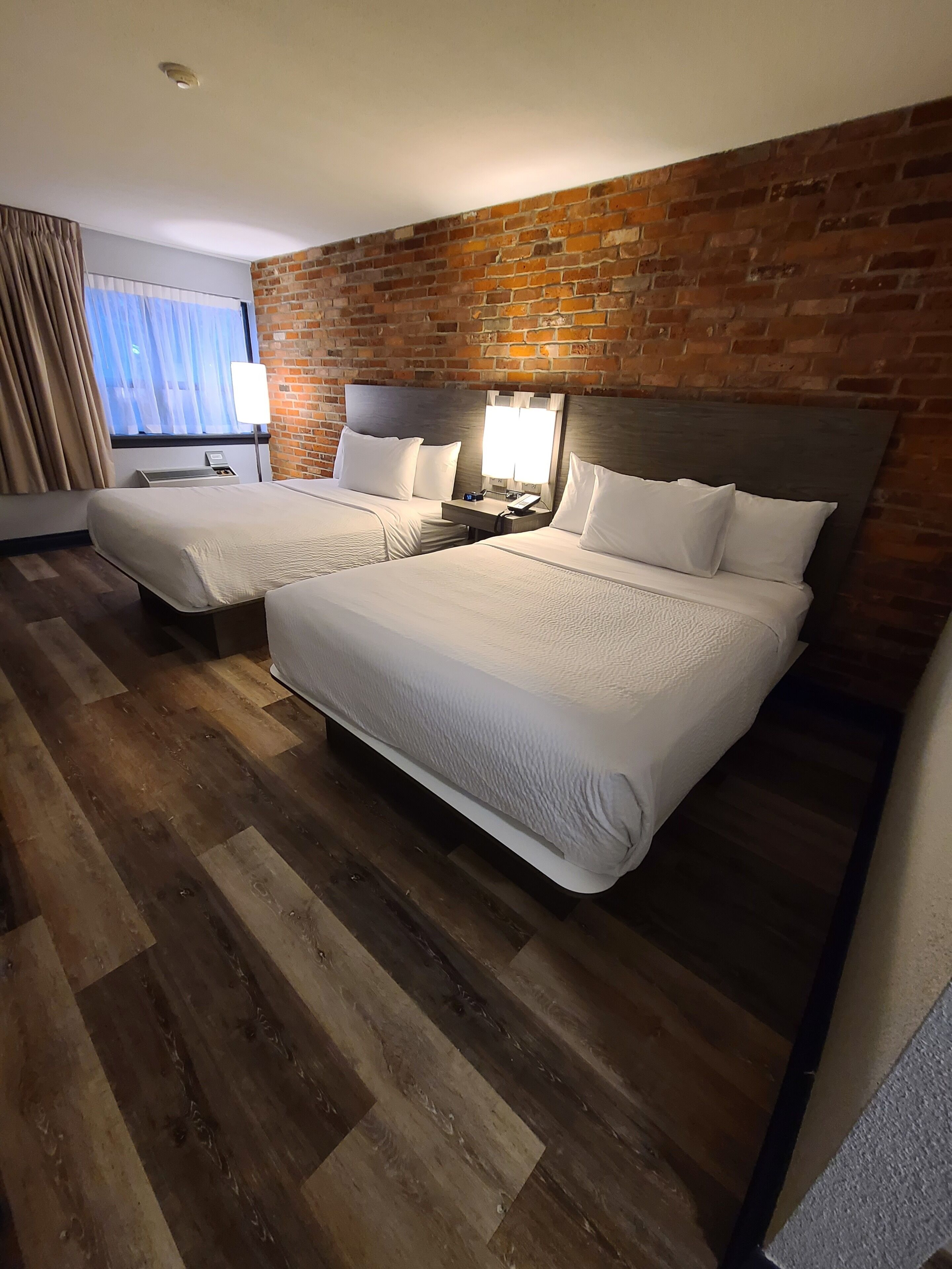 Hotellihuone, jossa on kaksi sänkyä, tiiliseinä ja puulattia.