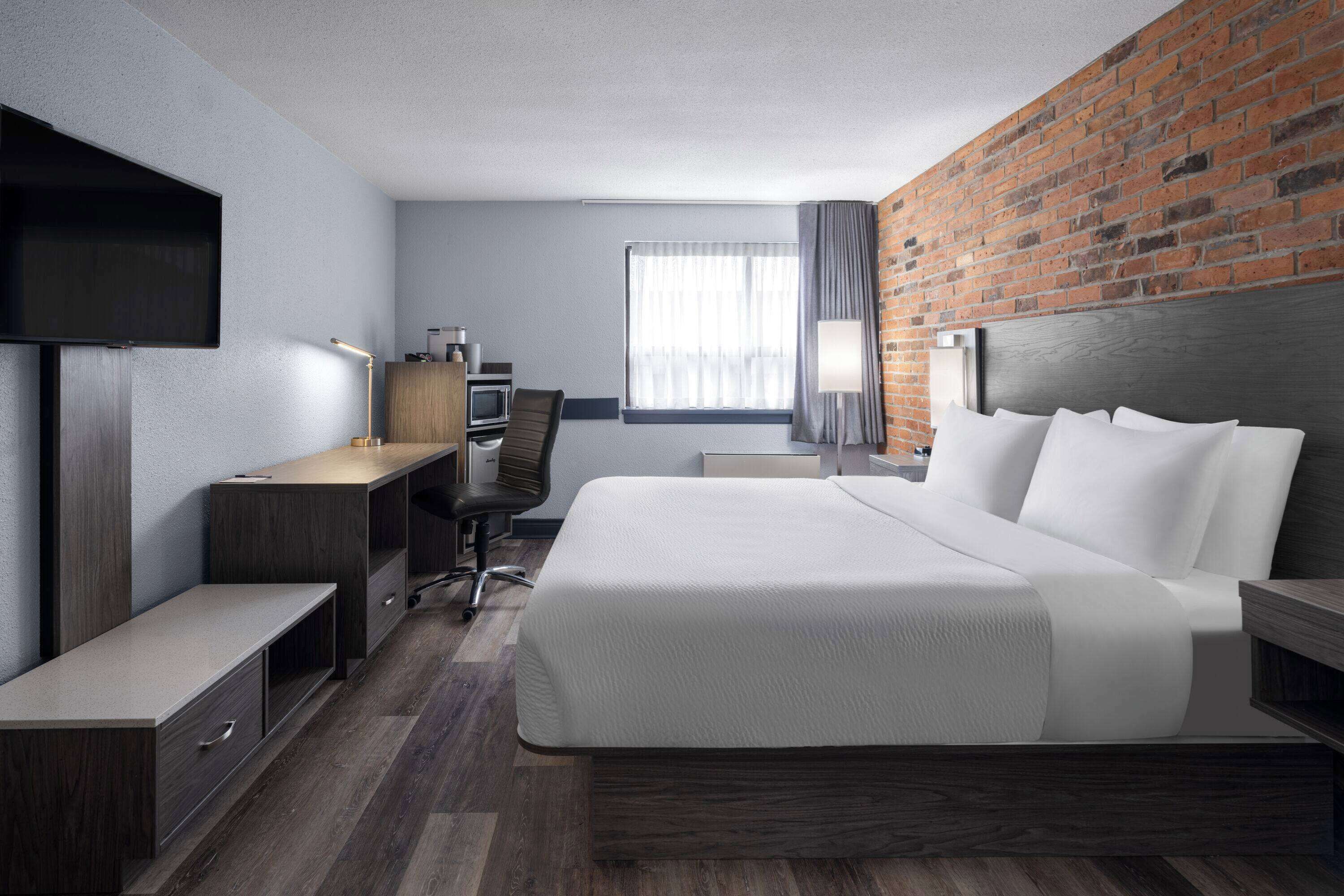 Ein Hotelzimmer mit Bett, Schreibtisch mit Stuhl, Fernseher und einem Fenster mit Vorhängen.