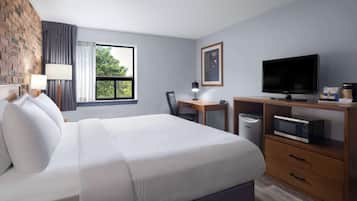 Een hotelkamer met een groot bed, een bureau met een computer, een televisie en uitzicht op groen.