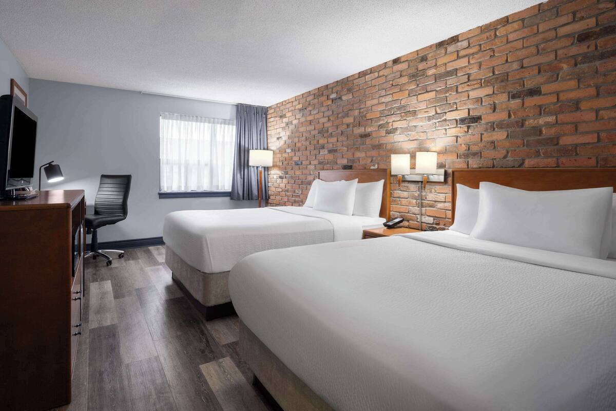 Une chambre d’hôtel avec deux lits, une télévision, un bureau et un mur en briques.