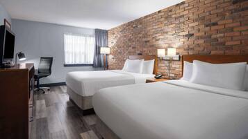 A hotel room with two beds, a TV, a desk, and a brick wall.