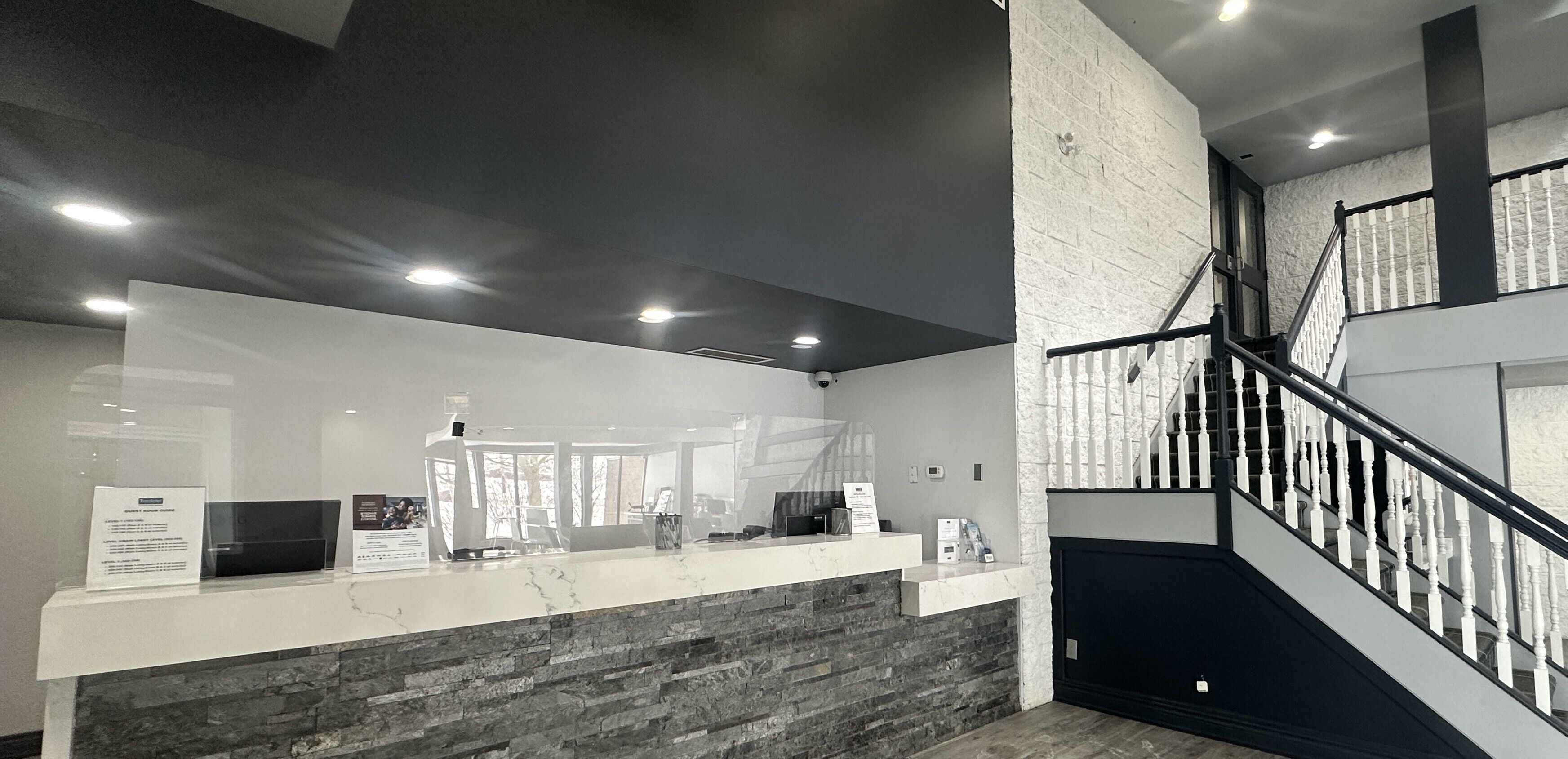 A reception area with a marble counter, a stone wall, a staircase with white balusters, and a dark ceiling.